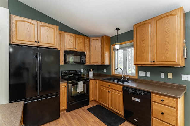 kitchen with black appliances, a sink, dark countertops, vaulted ceiling, and light wood-type flooring