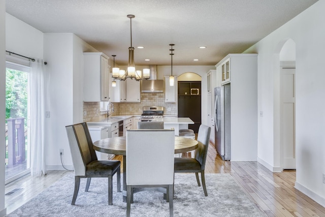 1730 Deephaven Dr, Woodbury, MN 55129 - dining space featuring light wood-style flooring, arched walkways, a chandelier, baseboards, and recessed lighting