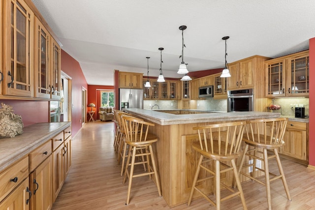 kitchen featuring stainless steel appliances, light wood-style floors, a large island, glass insert cabinets, and a kitchen breakfast bar