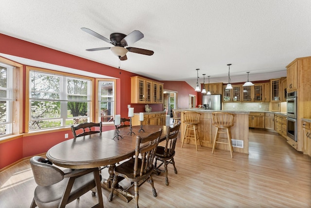 dining space with healthy amount of natural light, light wood-style flooring, a textured ceiling, and a ceiling fan