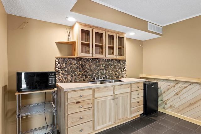 kitchen featuring black microwave, a sink, light brown cabinetry, a textured ceiling, and glass insert cabinets