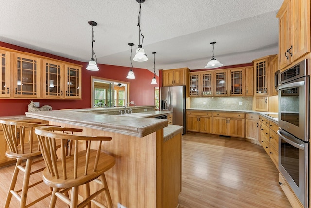 7715 217th Ave NE, Linwood Twp, MN 55092 - kitchen featuring stainless steel appliances, light wood-style flooring, a textured ceiling, a breakfast bar area, and a sink