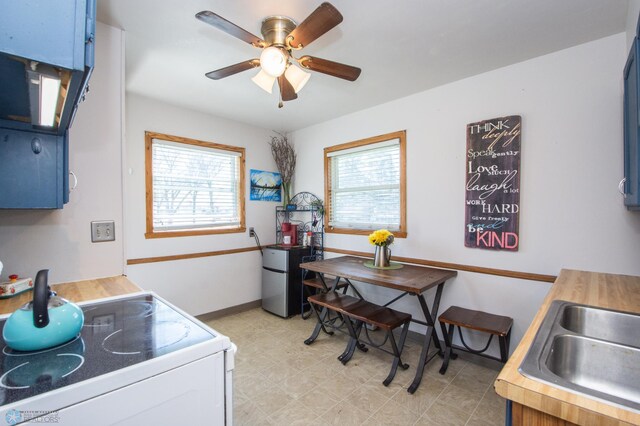 kitchen featuring white electric stove, freestanding refrigerator, a ceiling fan, baseboards, and blue cabinets
