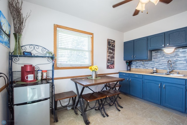 kitchen featuring blue cabinets, freestanding refrigerator, a sink, a ceiling fan, and decorative backsplash