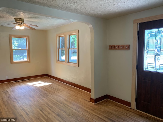 entrance foyer with a textured ceiling, arched walkways, healthy amount of natural light, wood finished floors, and a ceiling fan