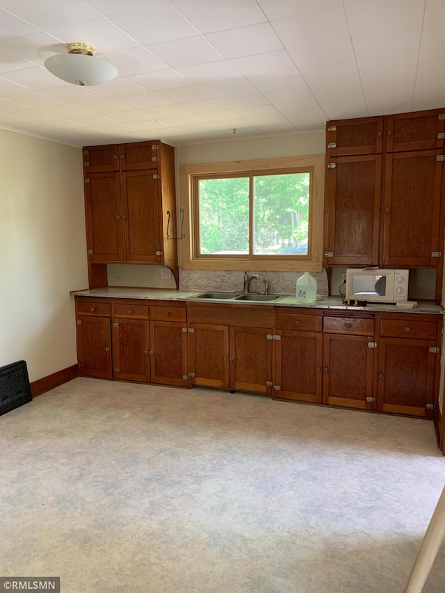 kitchen with a sink, white microwave, brown cabinets, baseboards, and light countertops