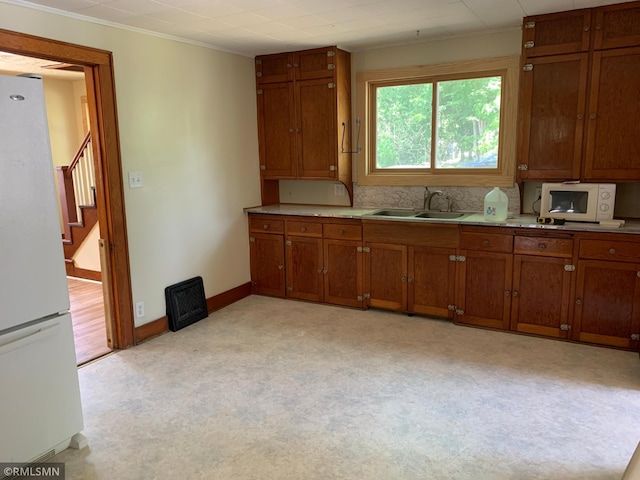 kitchen with white appliances, a sink, brown cabinets, light countertops, and crown molding