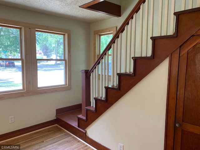 stairway featuring wood finished floors, baseboards, and a textured ceiling