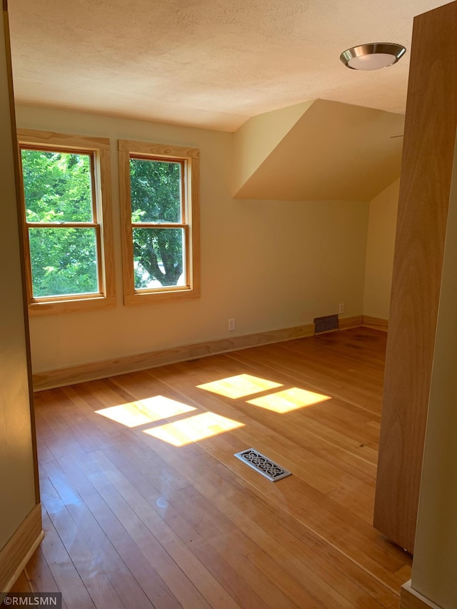 bonus room with hardwood / wood-style floors, a textured ceiling, and baseboards