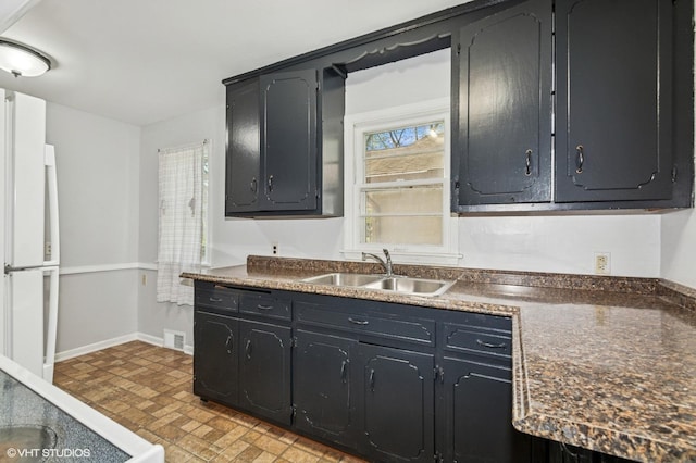 kitchen with a sink, dark countertops, brick patterned floors, and baseboards