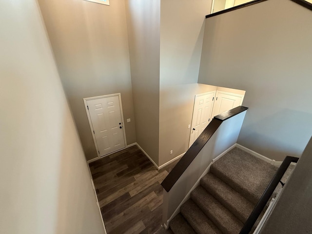 stairway featuring baseboards, wood finished floors, and a towering ceiling