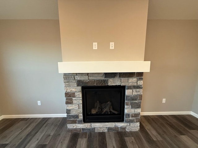 detailed view of wood finished floors, a stone fireplace, and baseboards