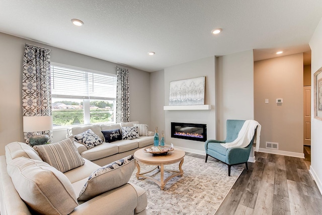 living room featuring wood finished floors, recessed lighting, a glass covered fireplace, baseboards, and a textured ceiling