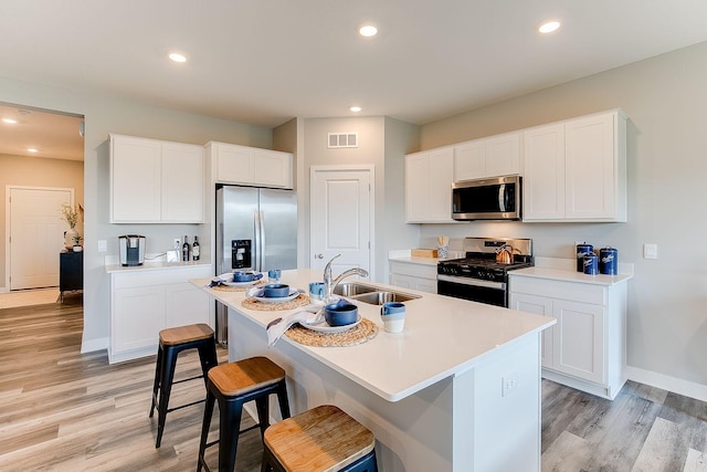 kitchen with stainless steel appliances, a sink, light wood-type flooring, a breakfast bar, and a kitchen island with sink