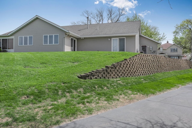 rear view of house featuring a lawn and a shingled roof