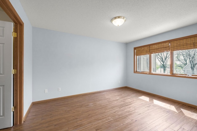 empty room with wood finished floors, a textured ceiling, and baseboards