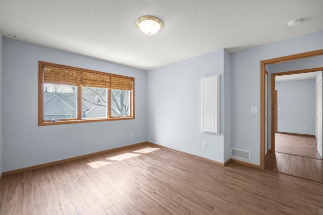 unfurnished room with wood finished floors, a textured ceiling, baseboards, and a smoke detector