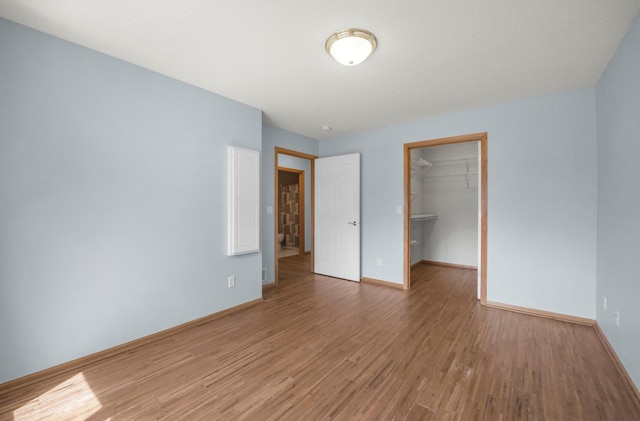 unfurnished bedroom featuring light wood-style floors, baseboards, a closet, and a walk in closet