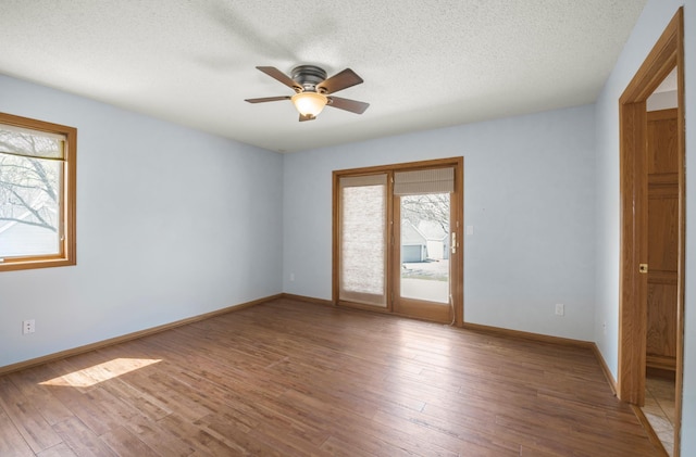 unfurnished room featuring plenty of natural light, ceiling fan, a textured ceiling, wood finished floors, and baseboards