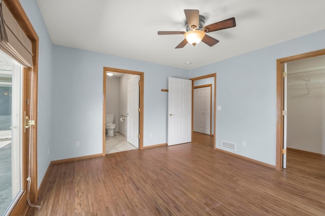 unfurnished bedroom featuring a spacious closet, wood finished floors, baseboards, and a closet