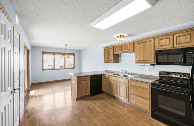 kitchen with black appliances, a sink, a peninsula, light wood-style floors, and a textured ceiling