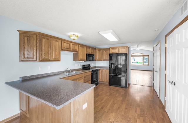 kitchen featuring black appliances, wood finished floors, a peninsula, and a sink