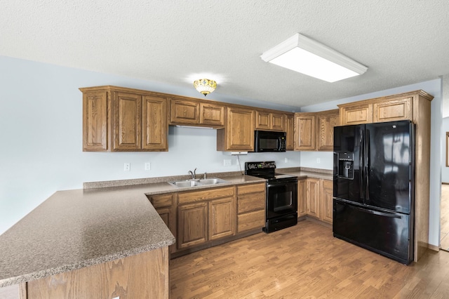 kitchen with black appliances, a sink, light wood-type flooring, a textured ceiling, and brown cabinets