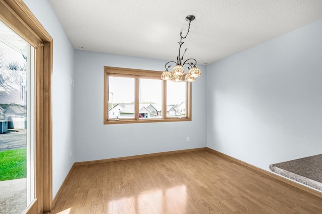 unfurnished dining area with a chandelier, light wood finished floors, and baseboards