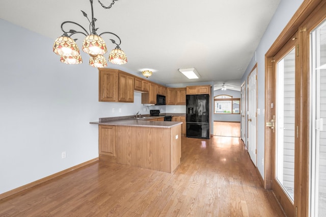 kitchen with black appliances, a peninsula, a sink, light wood-style flooring, and baseboards