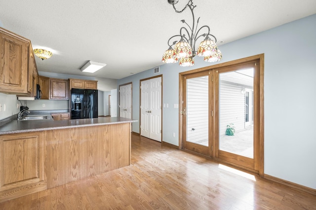 kitchen with black fridge, light wood-type flooring, a sink, baseboards, and a peninsula