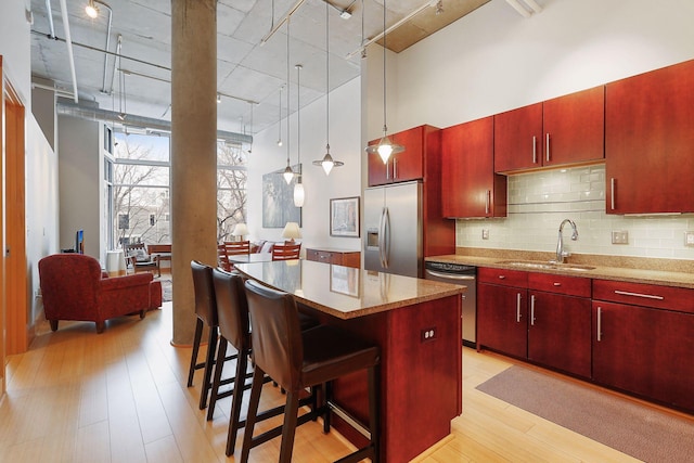 kitchen featuring appliances with stainless steel finishes, a high ceiling, light wood finished floors, tasteful backsplash, and track lighting