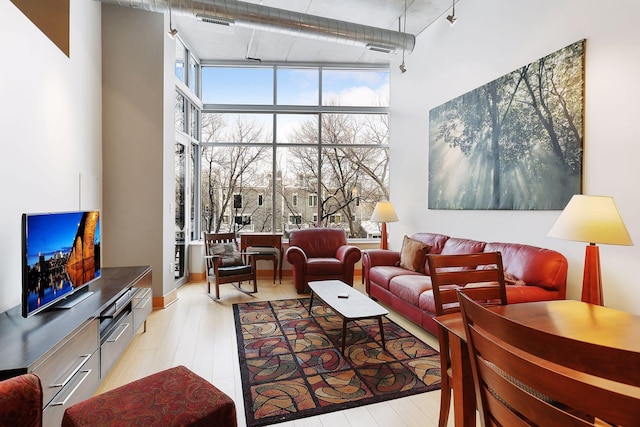 living area with floor to ceiling windows, rail lighting, light wood finished floors, and a high ceiling