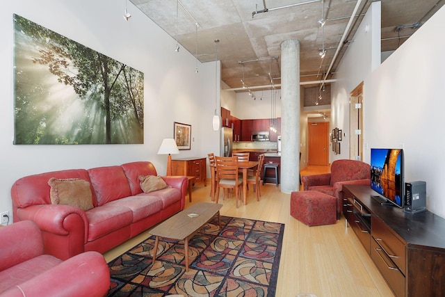 living room with rail lighting, light wood-type flooring, and a towering ceiling
