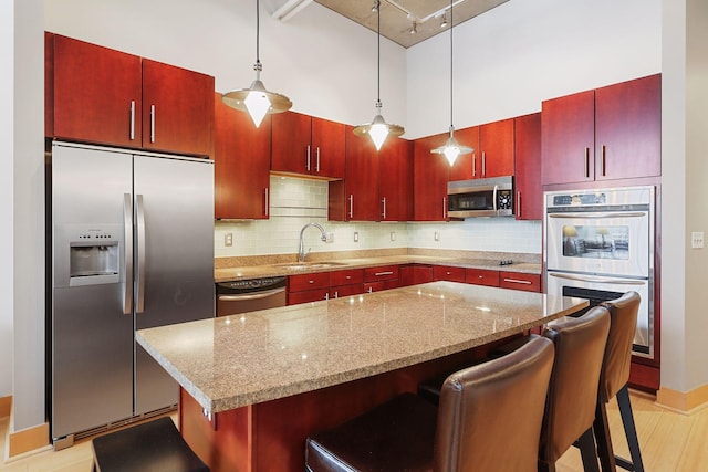 kitchen with appliances with stainless steel finishes, a sink, backsplash, reddish brown cabinets, and a high ceiling