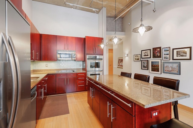 kitchen featuring appliances with stainless steel finishes, a towering ceiling, a kitchen island, light wood finished floors, and track lighting