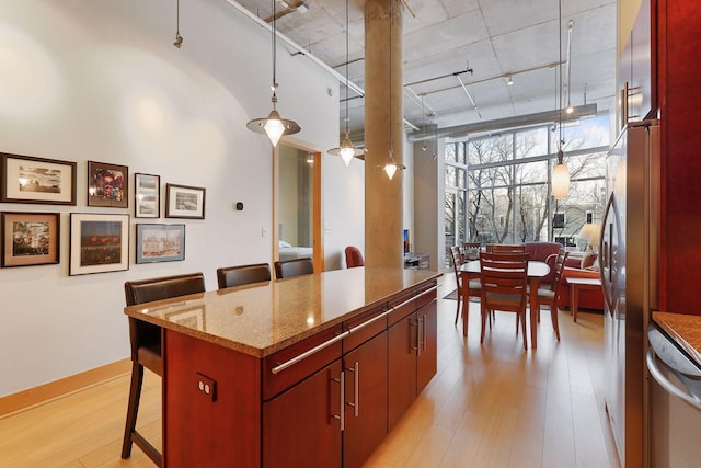 kitchen with light wood-style flooring, stainless steel dishwasher, a kitchen breakfast bar, stone counters, and a center island