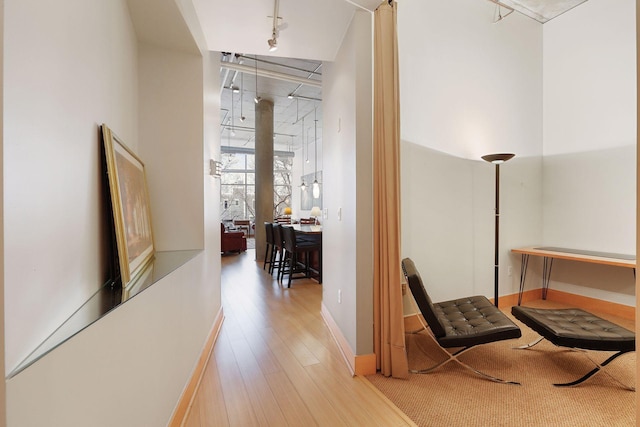 corridor featuring track lighting, wood finished floors, and baseboards