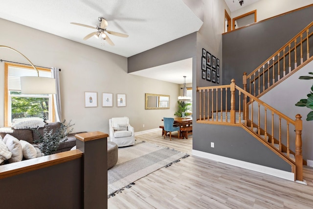 living room featuring a ceiling fan, wood finished floors, stairs, baseboards, and a chandelier