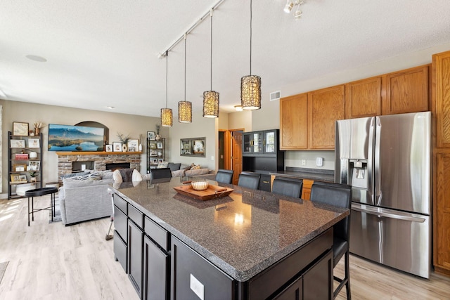 kitchen with stainless steel fridge, light wood-style flooring, a kitchen bar, a fireplace, and hanging light fixtures