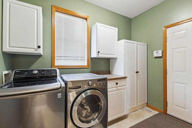 washroom with washer and dryer, cabinet space, a textured ceiling, and light tile patterned floors