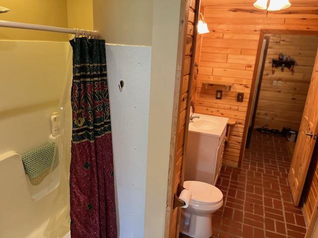 19323 Wendigo Park Rd, Harris Twp, MN 55744 - bathroom with brick patterned flooring, wood walls, curtained shower, vanity, and toilet