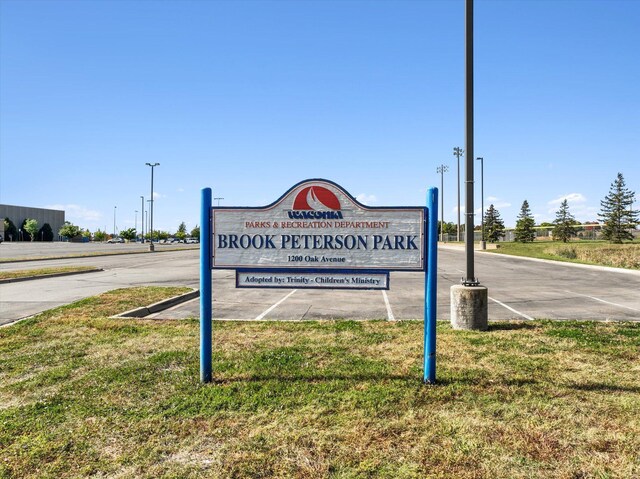 community sign with a lawn and uncovered parking