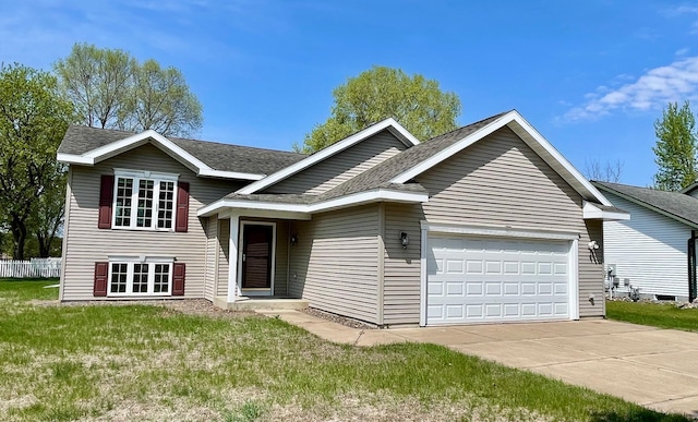 split level home with an attached garage, concrete driveway, a front lawn, and a shingled roof
