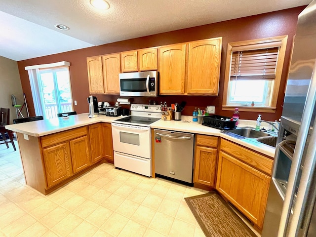 kitchen with stainless steel appliances, a peninsula, light countertops, a sink, and a textured ceiling