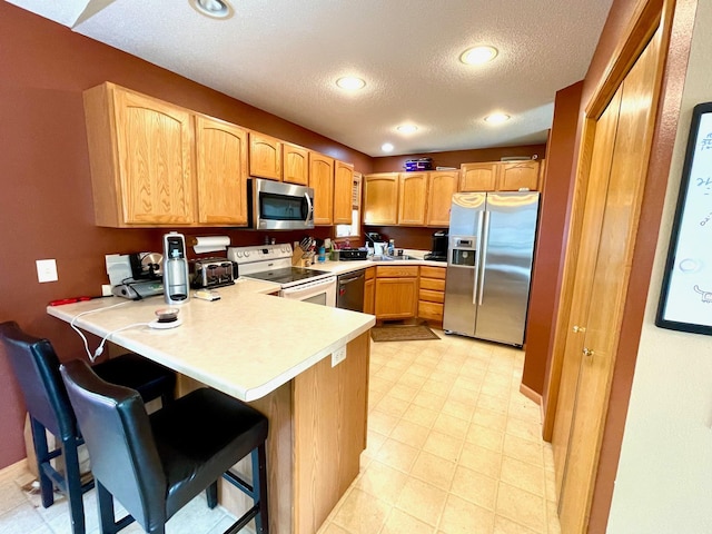 kitchen with appliances with stainless steel finishes, a peninsula, a kitchen breakfast bar, light countertops, and a textured ceiling
