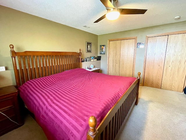 carpeted bedroom featuring two closets, a textured ceiling, and ceiling fan