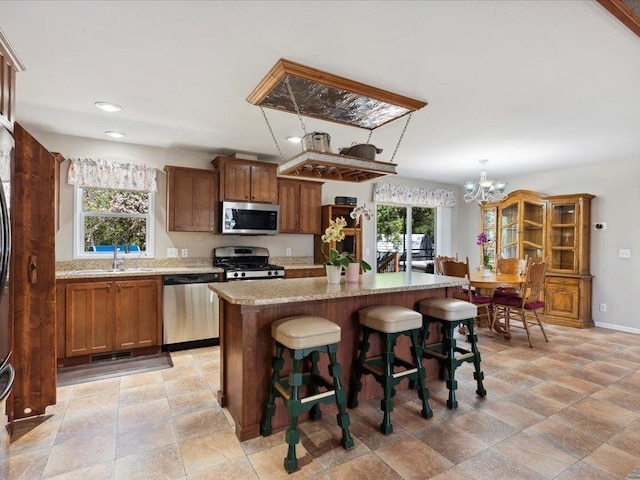 kitchen featuring appliances with stainless steel finishes, a sink, a kitchen island, brown cabinets, and recessed lighting
