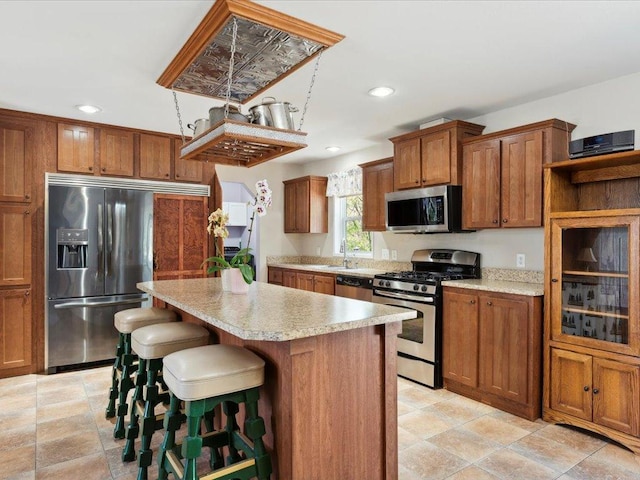 kitchen with appliances with stainless steel finishes, brown cabinetry, a kitchen island, recessed lighting, and light countertops