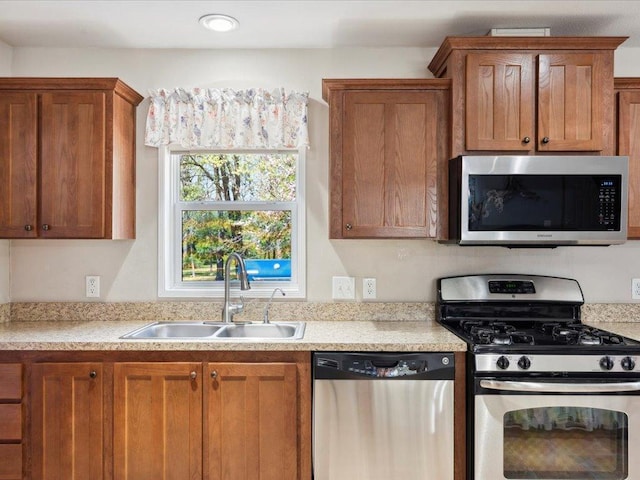 kitchen featuring stainless steel appliances, a sink, light countertops, and brown cabinetry