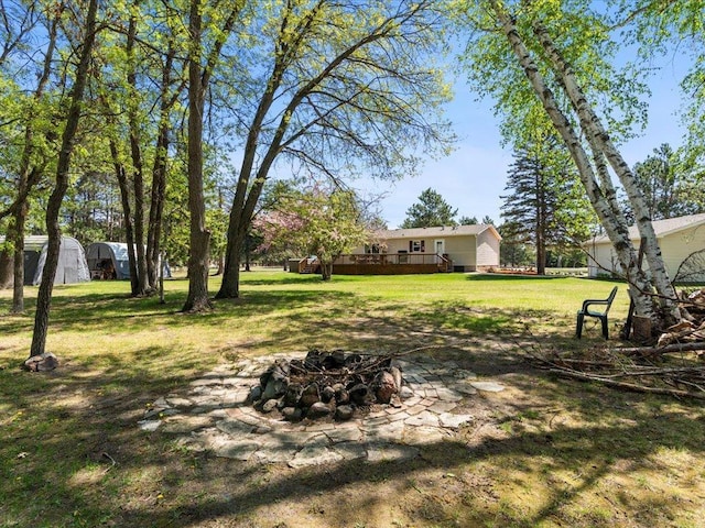 view of green lawn featuring an outdoor fire pit, a deck, a storage unit, and an outdoor structure
